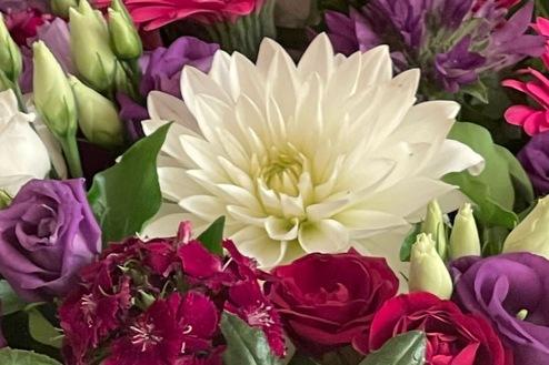 Nahaufnahme eines Blumengestecks in Rosa, Rot und Lila. Detailreiches Blumengesteck mit Dahlien, Rosen und Gerbera in kräftigen Rosa-, Rot- und Lilatönen, gestaltet von Ihrem Bestatter in Berlin für eine stilvolle Abschiednahme.